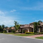 A quiet suburban street lined with houses, palm trees, and manicured lawns